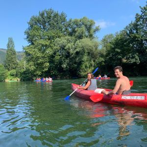 Un hombre y una mujer en una canoa roja sonríen a la cámara mientras practican kayak en un río durante su viaje en grupo con WeRoad.