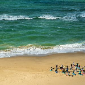 Un viaggio di gruppo WeRoad con una sessione di yoga su tappetini colorati su una spiaggia sabbiosa in riva all'oceano