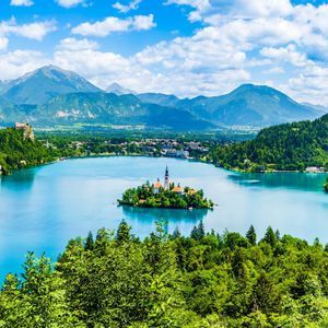 Una vista panorámica de una iglesia en una pequeña isla en medio de un lago azul tranquilo, rodeada de bosques y montañas.