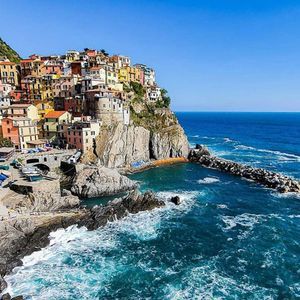 Una vista soleggiata di un colorato villaggio su una scogliera rocciosa che si affaccia su un mare blu profondo con una diga foranea in pietra.
