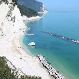 Una vista aerea di una spiaggia sabbiosa e appartata con acqua turchese, incastonata sotto una ripida scogliera bianca.