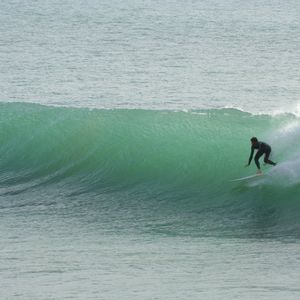 A surfer in a black wetsuit rides a surfboard on a large, green wave in the ocean.