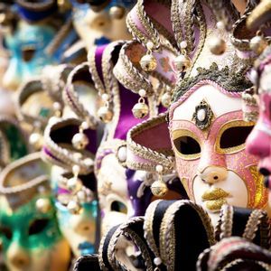Une rangée de masques vénitiens colorés et ornés exposés, avec un masque rose et blanc mis en valeur.