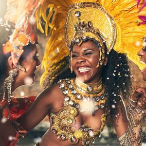 Trois femmes en costumes de carnaval élaborés et emplumés sourient et célèbrent tandis que des confettis tombent autour d'elles.