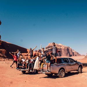 Un groupe WeRoad pose pour une photo à l'arrière d'un pick-up dans un vaste désert entouré de formations rocheuses rouges.