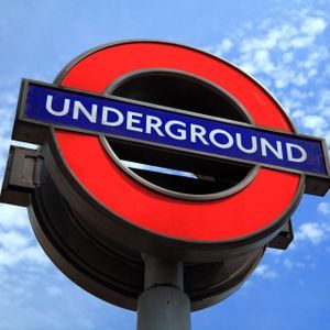 El letrero circular rojo del metro de Londres visto desde abajo contra un cielo azul con nubes blancas.