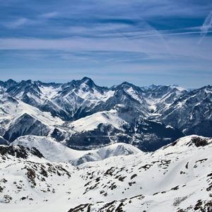 A panoramic view of a vast, snow-covered mountain range with jagged peaks under a clear blue sky.