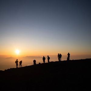 Un gruppo WeRoad in viaggio, stagliato su una cima di montagna, osserva l'alba su un mare di nuvole.