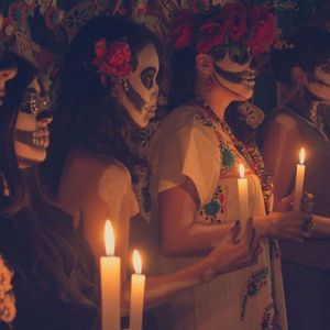 A WeRoad group trip of women with skull face paint and flower crowns holding lit candles in a dimly lit room.