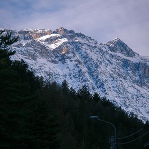 Il sole illumina la vetta di una montagna aspra e innevata che domina una scura foresta di conifere.