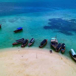 Eine Luftaufnahme von Holzbooten, die an einem weißen Sandstrand vor türkisfarbenem und tiefblauem Meerwasser liegen.