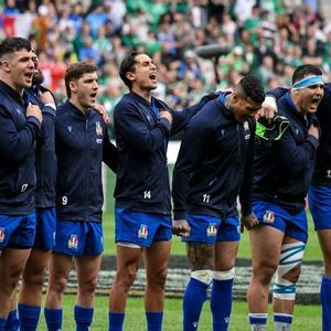 La nazionale italiana di rugby e un giovane ragazzo sono in fila su un campo, cantando con passione prima di una partita.