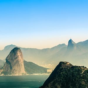 Una vista mozzafiato di montagne nebbiose che si ergono dall'oceano, con una distinta cima conica e una statua lontana su una vetta.