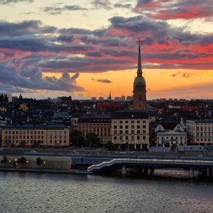 Il profilo di una città con un alto campanile di chiesa si staglia contro un tramonto colorato su uno specchio d'acqua.
