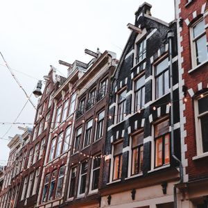 Una vista dal basso di tradizionali edifici a frontone in mattoni, disposti in fila, con ghirlande di luci sospese sopra contro un cielo nuvoloso.