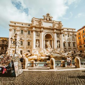 Une fontaine ornée en marbre blanc sur une place de ville par une journée ensoleillée, avec un stand de souvenirs au premier plan sur les pavés.