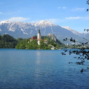 Veduta di un'isoletta con chiesa su un lago, circondata da montagne innevate sotto un cielo azzurro.