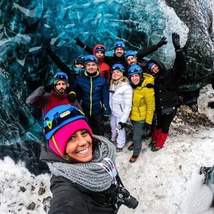 Un viaggio di gruppo WeRoad, con caschi e giacche invernali, sorride per un selfie all'interno di una grotta di ghiaccio blu traslucida.