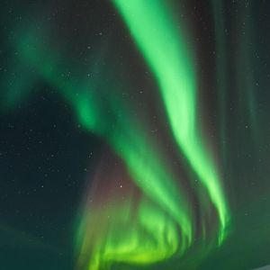 Bright green bands of the aurora borealis glow in the starry night sky above a snowy mountain range.