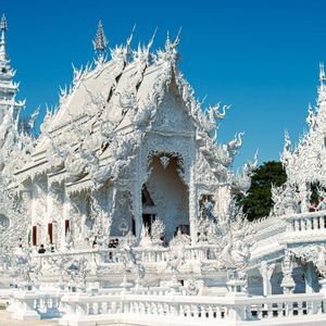 An ornate white temple with intricate carvings and spires stands under a clear blue sky.