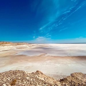 Una vista grandangolare di una sconfinata distesa di sale bianca che si estende fino all'orizzonte sotto un cielo blu intenso, ripresa da un belvedere roccioso.