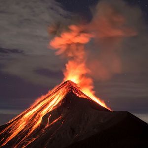 A volcano erupts at night, with glowing lava flowing down its dark slopes under a starry sky.