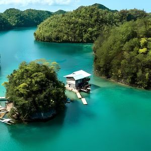 Una moderna casa su palafitte sorge su una piccola isola in un fiume turchese, circondata da lussureggianti colline ricoperte di giungla.