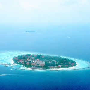 Vue aérienne d'une petite île tropicale luxuriante avec un complexe hôtelier, entourée d'eaux turquoises et de l'océan d'un bleu profond.