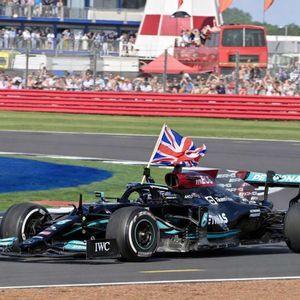 A black Formula 1 race car with a British flag attached drives around a track in front of spectators in the stands.