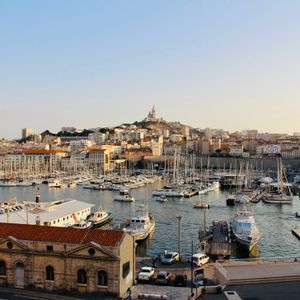 Un vaste port rempli de voiliers et de yachts, avec une ville historique et une basilique sur une colline lointaine.