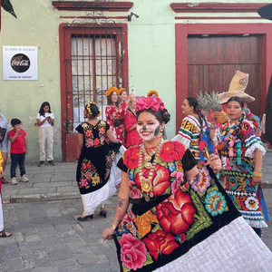 Une femme au maquillage de crâne, vêtue d'une robe colorée et brodée, danse lors d'une parade de rue avec un groupe WeRoad.