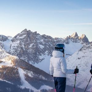Due sciatori di un viaggio di gruppo WeRoad si fermano ad ammirare una catena montuosa innevata e illuminata dal sole.