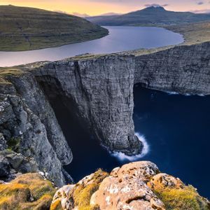 Un grande lago si trova sul bordo di un'alta scogliera, affacciato sul profondo oceano blu, con verdi colline ondulate in lontananza.