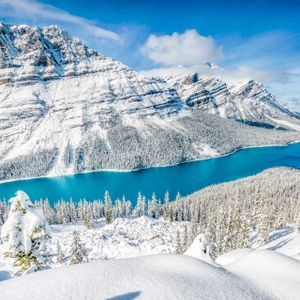 Un vivace lago turchese circondato da una vasta foresta innevata ai piedi di grandi montagne innevate.