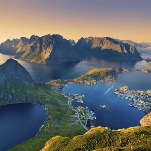 Panoramablick auf Küstendörfer auf grünen Inseln, umgeben von Fjorden und zerklüfteten Bergen unter goldenem Himmel.