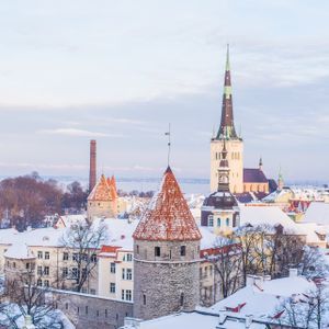Luftaufnahme der verschneiten Dächer einer historischen Stadt, mit markanten Steintürmen und einem Kirchturm vor blassem Himmel.