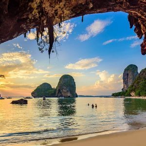 Ein Blick aus einer Meereshöhle auf einen tropischen Strand mit Kalksteinkarsten und Booten bei Sonnenuntergang.