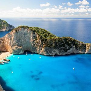 Una vista aerea di una cala appartata con un relitto su una spiaggia di sabbia bianca, circondata da scogliere e acqua turchese con barche.