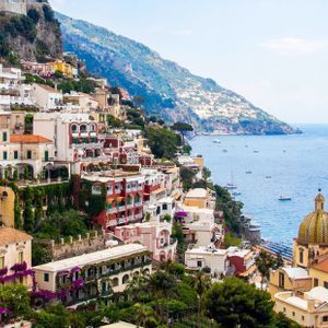 Una vista panoramica di una colorata città costiera costruita su una scogliera, che si affaccia su un mare blu con tante barche.