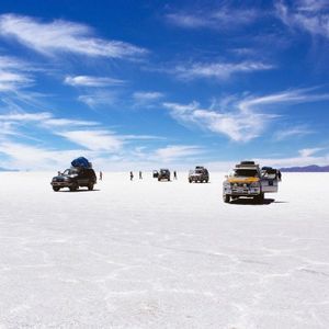 Un viaggio di gruppo WeRoad con diversi veicoli fuoristrada si è fermato su una vasta piana di sale bianca sotto un cielo azzurro brillante con nuvole sottili.