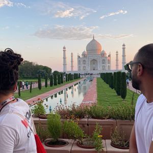 A long reflecting pool leads to a large white marble mausoleum with minarets, surrounded by gardens where people are walking.
