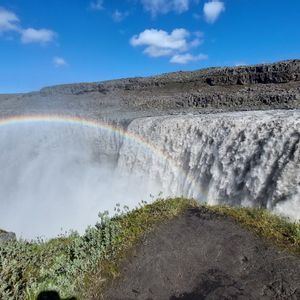 Un arcobaleno si inarca sulla nebbia di una potente cascata che precipita in un canyon roccioso sotto un cielo azzurro e limpido.