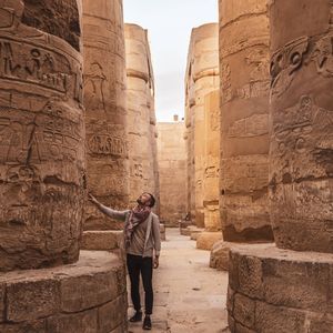 A man stands in an ancient temple hall, looking up at the hieroglyphs carved into the massive stone columns.