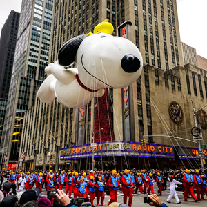 Un grande pallone di Snoopy fluttua sopra una parata in una strada cittadina di fronte alla Radio City Music Hall, con la folla che osserva.