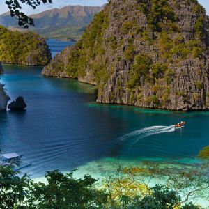 A motorboat sails through a turquoise lagoon surrounded by steep, jungle-covered cliffs.
