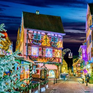 Una strada acciottolata con edifici a graticcio illuminati a festa con luci e ghirlande natalizie di notte.