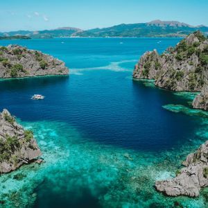 Vista aerea di una barca che naviga in una laguna turchese affiancata da grandi formazioni rocciose coperte dalla giungla.