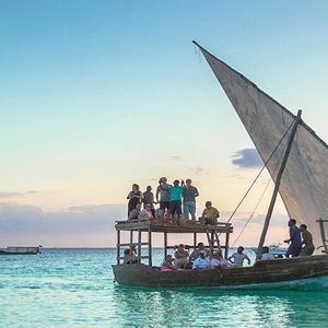 Eine WeRoad Gruppenreise, die bei Sonnenuntergang auf einem traditionellen zweistöckigen Holz-Dhow-Boot auf türkisfarbenem Wasser segelt.