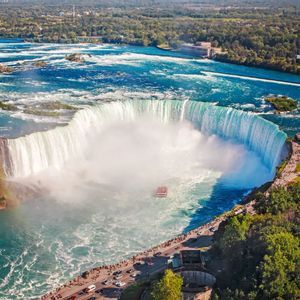 Vue aérienne d'une immense cascade en forme de fer à cheval avec un bateau touristique naviguant dans les eaux brumeuses à sa base.
