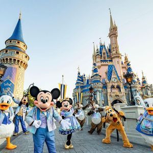 Mickey Mouse y amigos con atuendo formal posan juntos en un puente con un gran castillo de cuento de hadas de fondo.